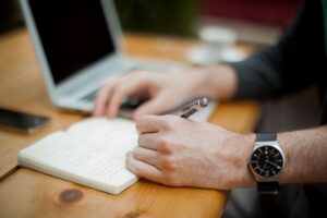 hands taking notes on a desk with a computer